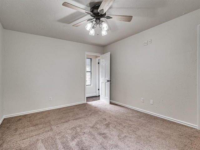carpeted empty room featuring a ceiling fan and baseboards