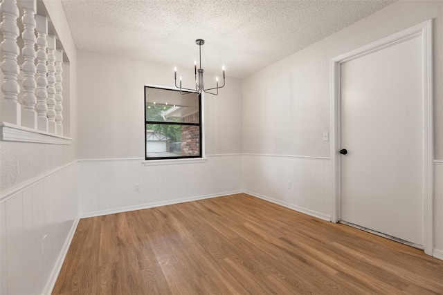 unfurnished room with a textured ceiling, wood finished floors, and a chandelier