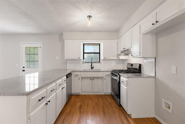 kitchen featuring a textured ceiling, a sink, a peninsula, under cabinet range hood, and stainless steel appliances