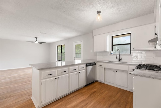 kitchen with a textured ceiling, dishwasher, a sink, a peninsula, and light wood-style flooring