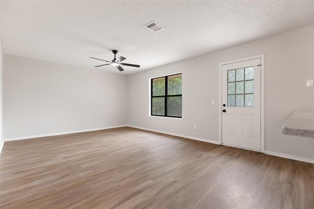 empty room featuring visible vents, wood finished floors, baseboards, a textured ceiling, and a ceiling fan
