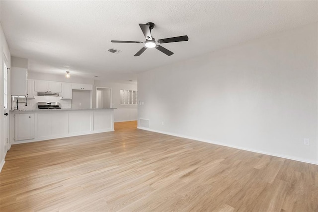unfurnished living room with light wood-type flooring, baseboards, ceiling fan, and visible vents