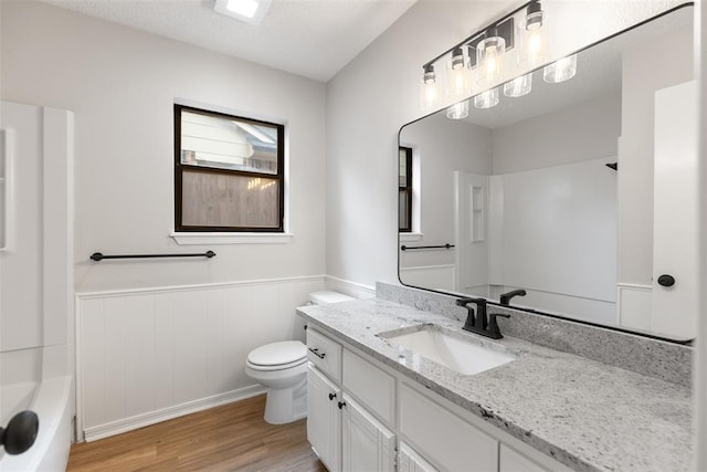 full bath featuring wainscoting, vanity, toilet, a tub, and wood finished floors