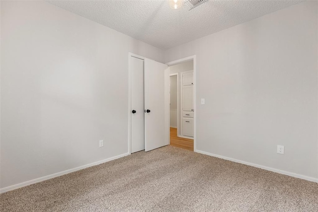 spare room with carpet floors, baseboards, a textured ceiling, and visible vents