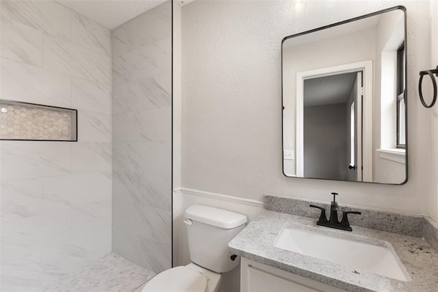 full bathroom with toilet, tiled shower, and vanity