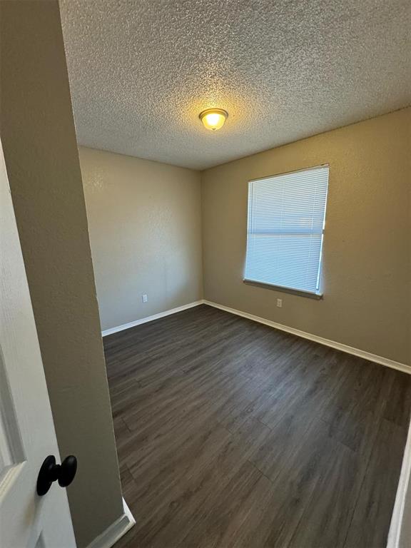 3509 N Nesbitt Ave, Oklahoma City, OK 73112 - empty room with dark wood-type flooring, a textured ceiling, and baseboards
