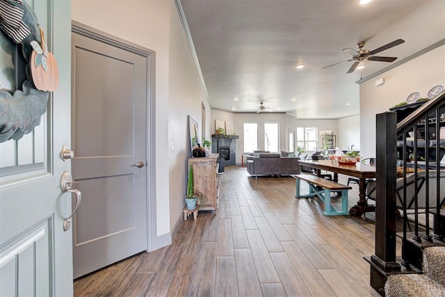 foyer entrance with a ceiling fan, ornamental molding, wood finished floors, stairs, and baseboards