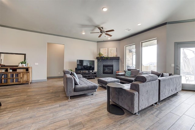 living room featuring crown molding, ceiling fan, light wood finished floors, a brick fireplace, and baseboards