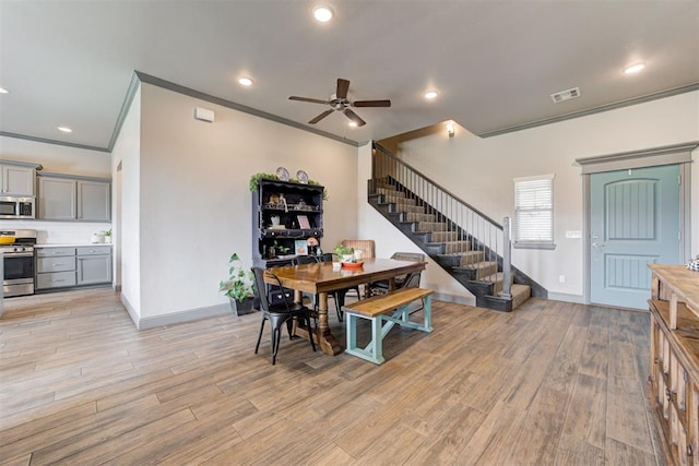 dining room featuring stairway, ceiling fan, ornamental molding, baseboards, and light wood-style flooring