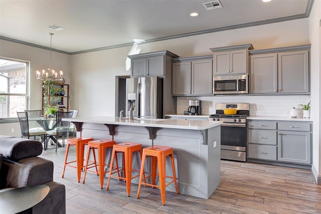 kitchen with stainless steel appliances, gray cabinets, crown molding, a kitchen breakfast bar, and recessed lighting