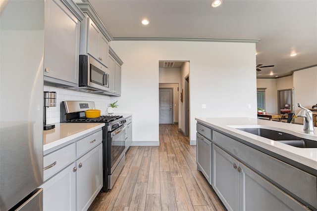 kitchen featuring stainless steel appliances, gray cabinets, a sink, light countertops, and recessed lighting