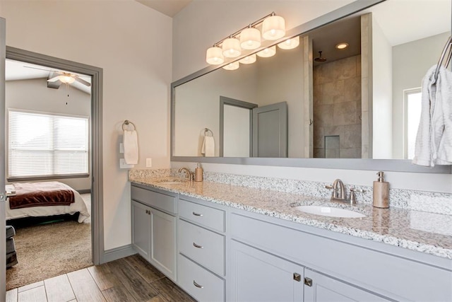 bathroom with ceiling fan, double vanity, a tile shower, and wood finished floors
