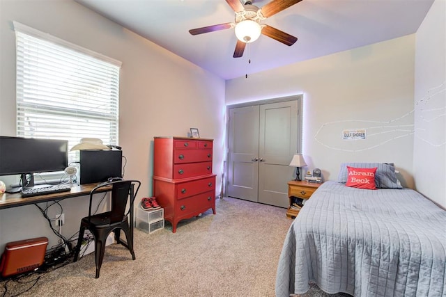 bedroom featuring light colored carpet, a ceiling fan, a closet, and a desk