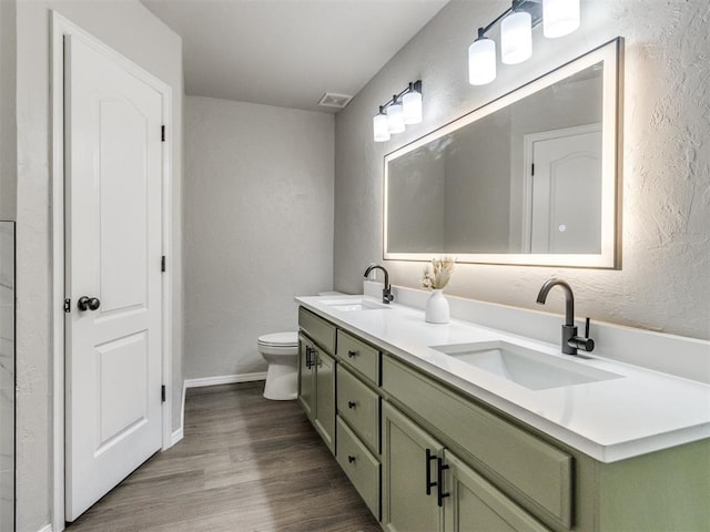 bathroom featuring toilet, a textured wall, a sink, and wood finished floors