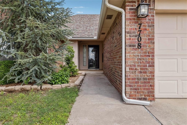 entrance to property featuring brick siding, a shingled roof, and a garage