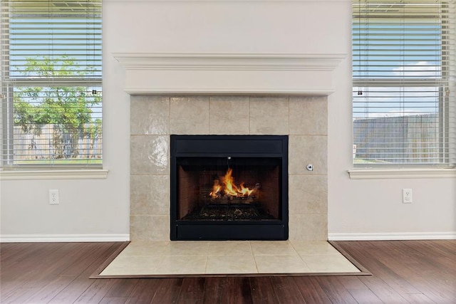 details with a tiled fireplace, baseboards, and wood finished floors