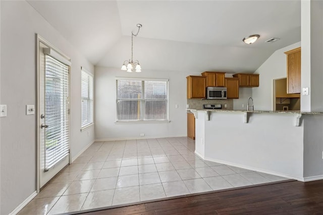 kitchen with stainless steel microwave, vaulted ceiling, a kitchen bar, and brown cabinetry