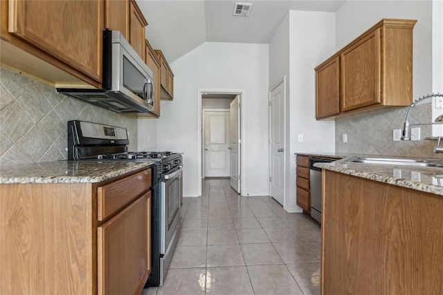 kitchen featuring visible vents, appliances with stainless steel finishes, a sink, light stone counters, and lofted ceiling