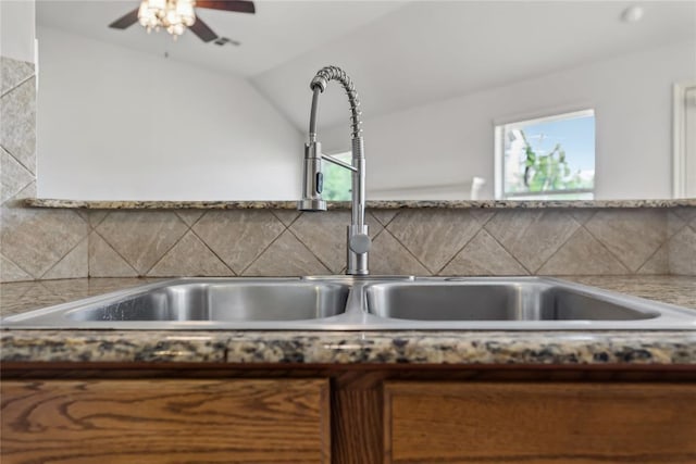 kitchen featuring ceiling fan, a sink, visible vents, backsplash, and vaulted ceiling