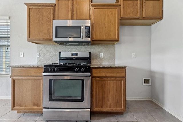 kitchen featuring baseboards, decorative backsplash, appliances with stainless steel finishes, and light stone counters