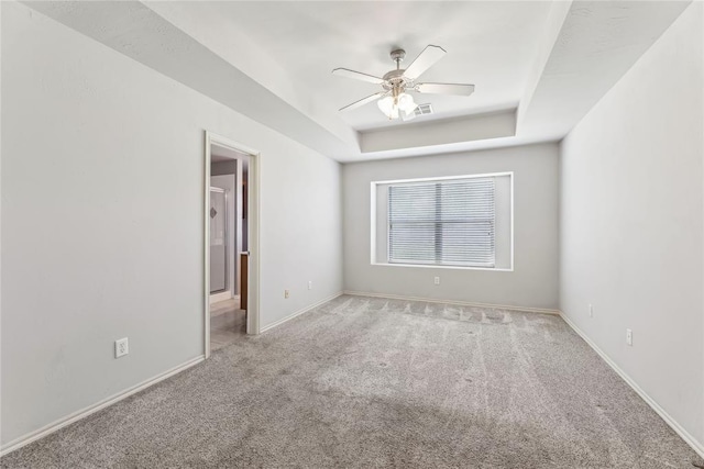 spare room featuring ceiling fan, a raised ceiling, carpet floors, baseboards, and visible vents