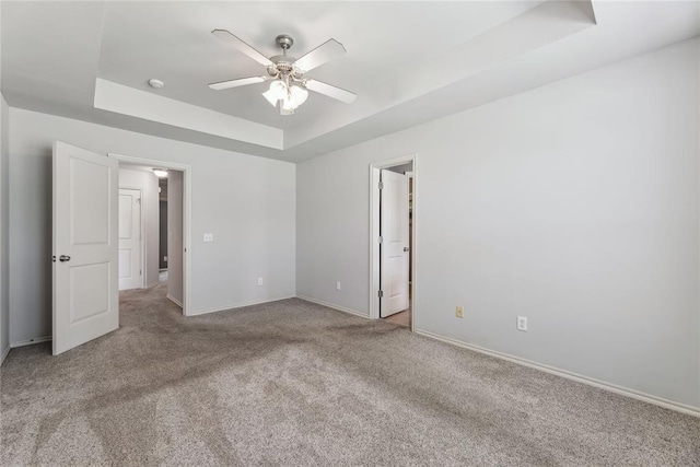 unfurnished bedroom with baseboards, ceiling fan, a tray ceiling, and carpet flooring