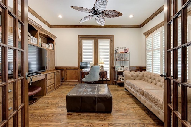 living room featuring crown molding, a wainscoted wall, ceiling fan, and built in desk