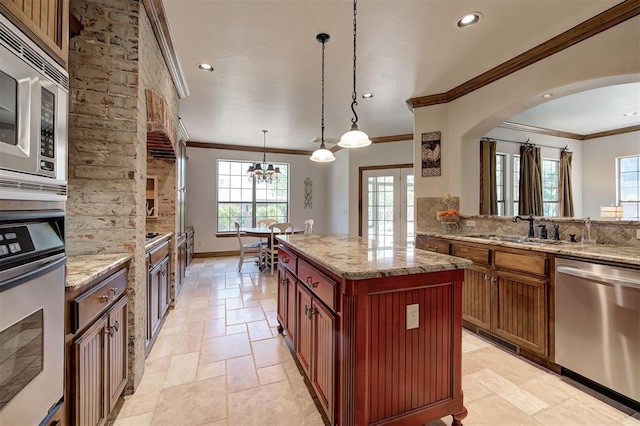 kitchen with stone tile flooring, ornamental molding, arched walkways, a sink, and appliances with stainless steel finishes