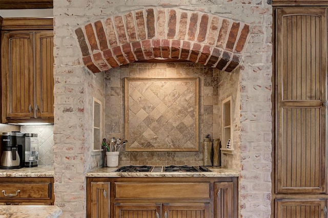 details featuring stainless steel gas cooktop, backsplash, and brown cabinets