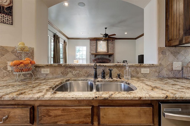 kitchen featuring crown molding, a sink, a ceiling fan, and light stone counters