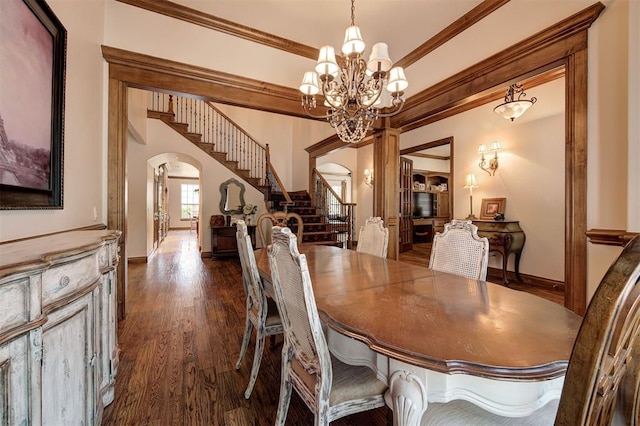 dining room featuring arched walkways, a chandelier, dark wood-type flooring, ornamental molding, and stairway