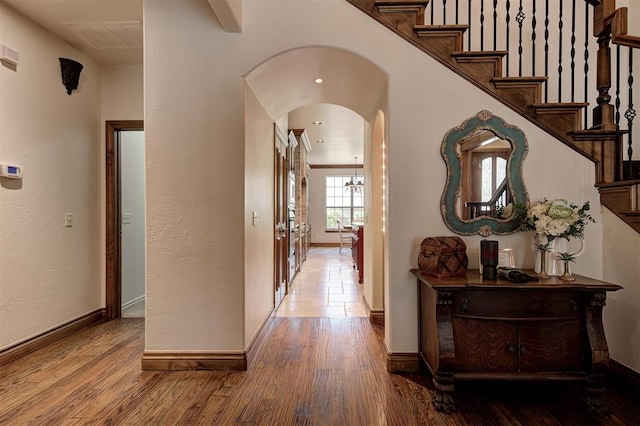 corridor featuring arched walkways, baseboards, and wood finished floors