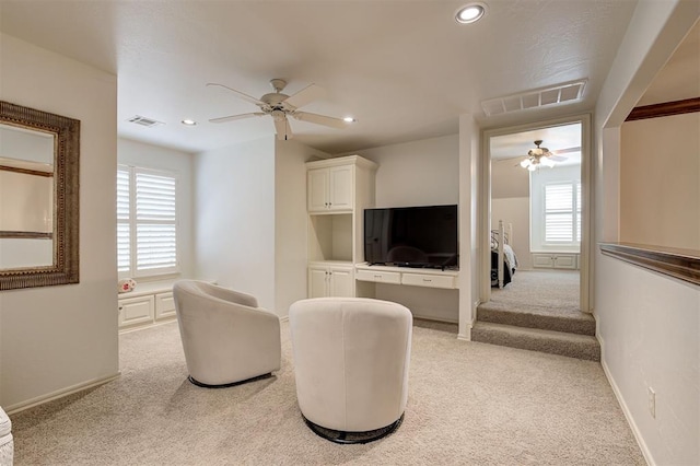 living area with a healthy amount of sunlight, ceiling fan, visible vents, and light colored carpet