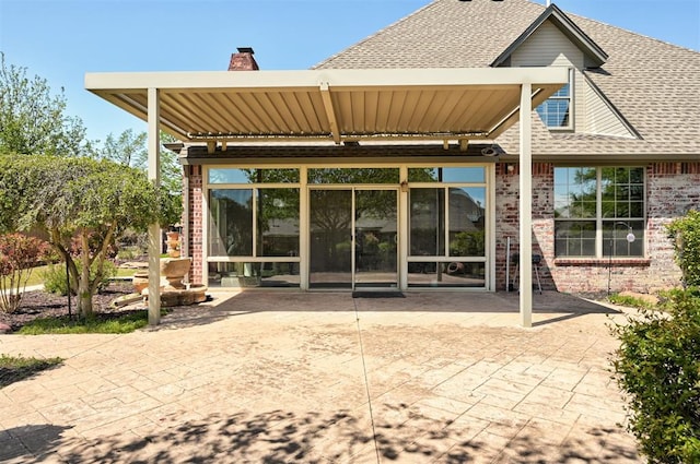 back of property featuring brick siding, a shingled roof, a chimney, and a patio