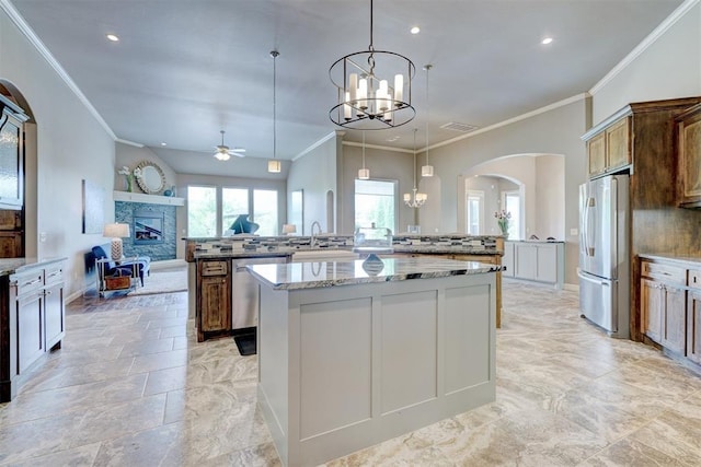kitchen with appliances with stainless steel finishes, a fireplace, arched walkways, ceiling fan with notable chandelier, and a spacious island
