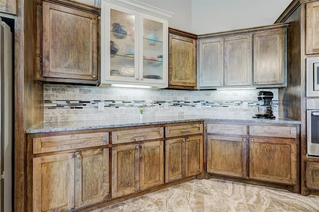 kitchen with backsplash, stainless steel appliances, light stone countertops, and glass insert cabinets