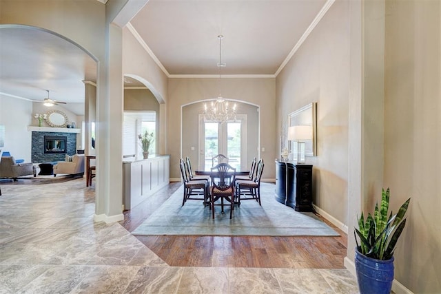 dining space with crown molding, arched walkways, a fireplace, and ceiling fan with notable chandelier