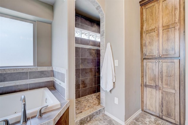 bathroom featuring plenty of natural light, baseboards, walk in shower, and a tub with jets