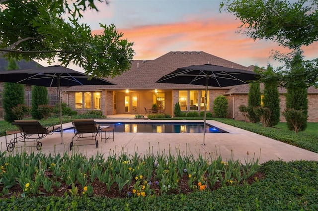 back of property at dusk featuring brick siding, an outdoor pool, and a patio area
