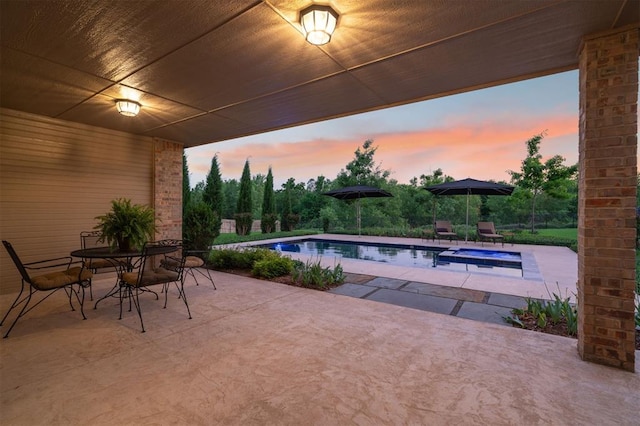 patio terrace at dusk featuring an in ground hot tub, outdoor dining area, and an outdoor pool