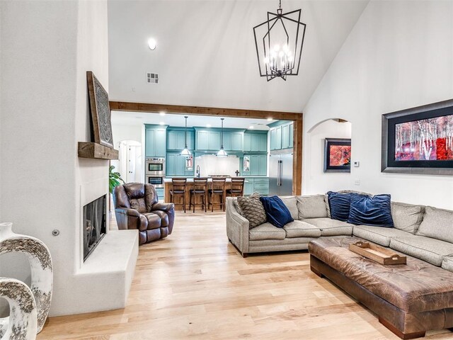living area with light wood-style floors, high vaulted ceiling, a fireplace with raised hearth, and visible vents