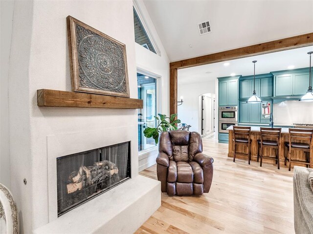 living room with visible vents, recessed lighting, a fireplace with raised hearth, light wood finished floors, and vaulted ceiling