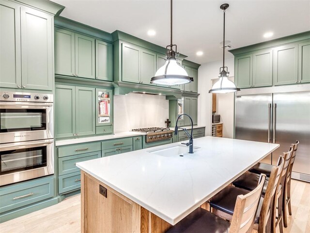 kitchen featuring a breakfast bar area, green cabinetry, a sink, hanging light fixtures, and stainless steel appliances