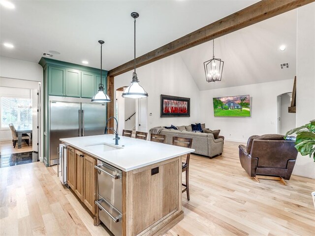 kitchen featuring a sink, light wood finished floors, an island with sink, vaulted ceiling with beams, and visible vents