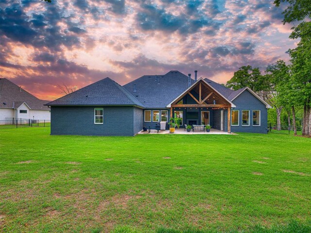 back of house at dusk featuring fence, a yard, and a patio area