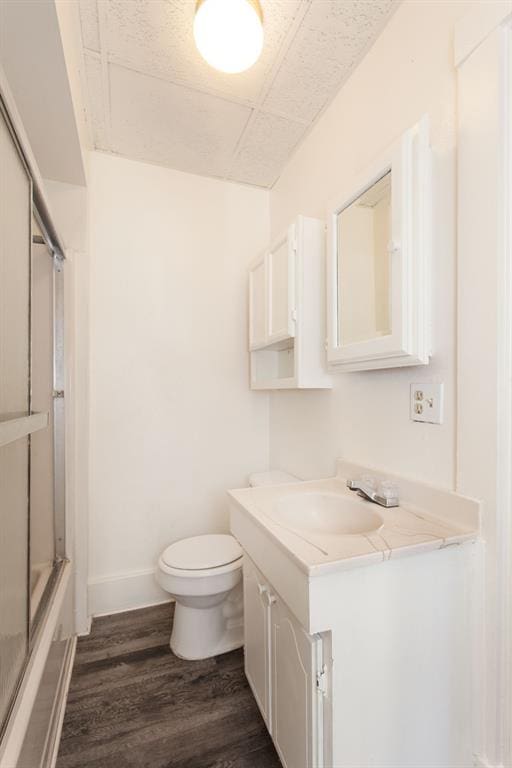 bathroom with vanity, wood finished floors, toilet, baseboards, and combined bath / shower with glass door