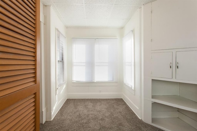 carpeted empty room featuring baseboards and a drop ceiling
