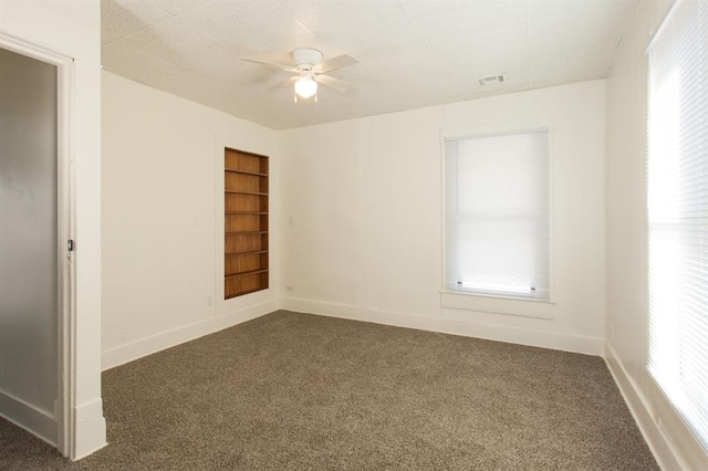 spare room featuring built in features, baseboards, dark colored carpet, and visible vents