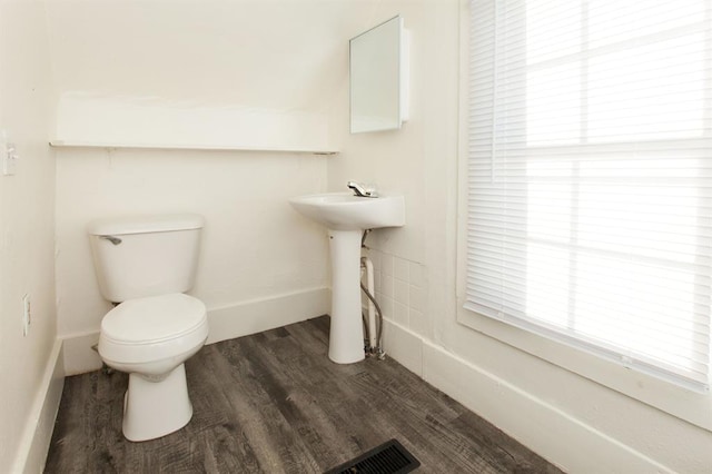 half bath with visible vents, wood finished floors, toilet, baseboards, and a sink