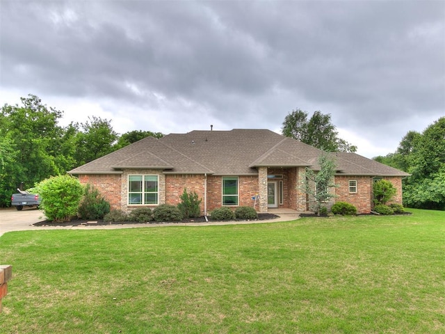 ranch-style home featuring brick siding, roof with shingles, and a front yard